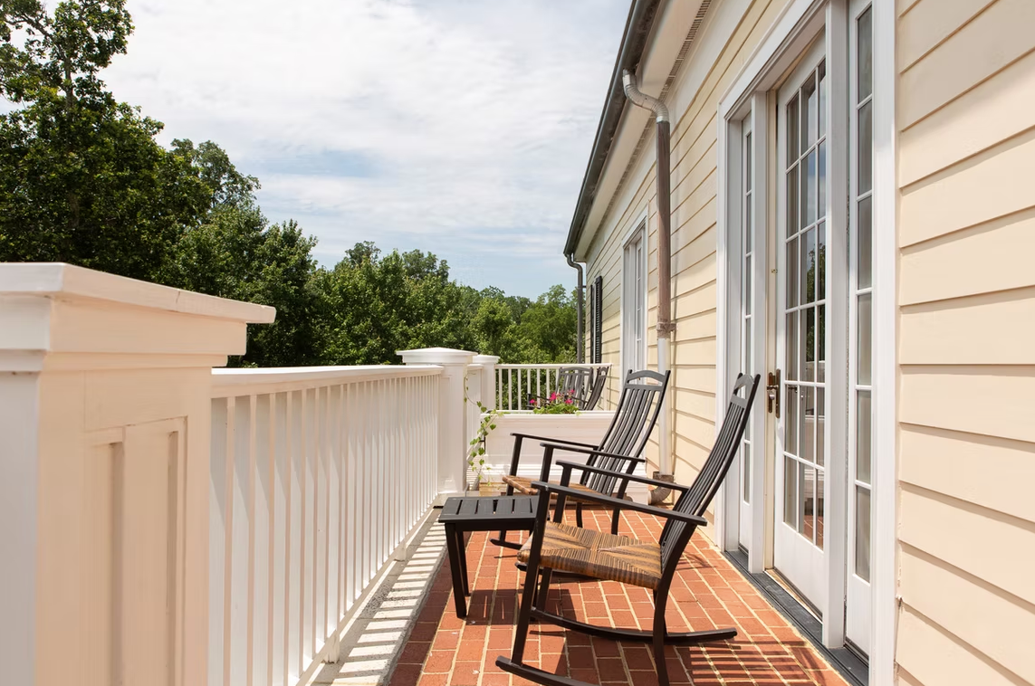 Patio with black chairs beside a cream house and white railing overlooking trees