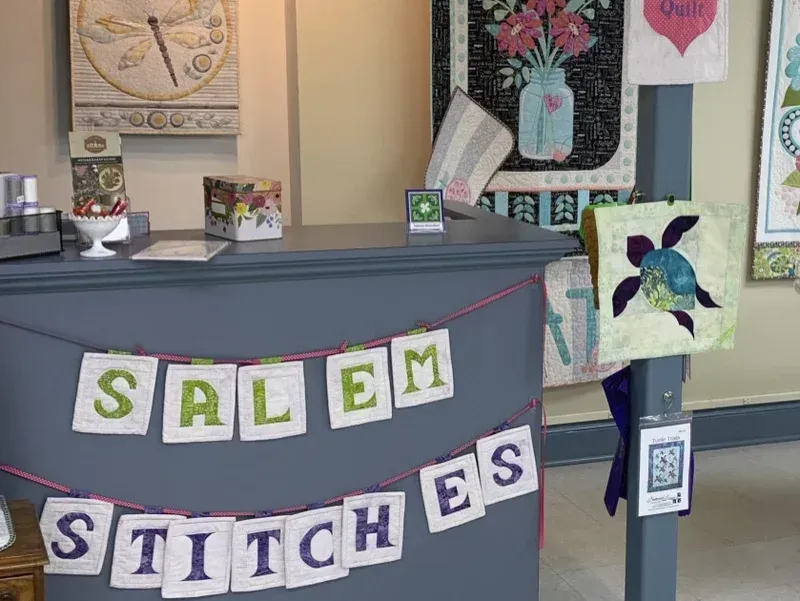 “SALEM STITCHES” banner at a craft booth with quilts and handmade items on display