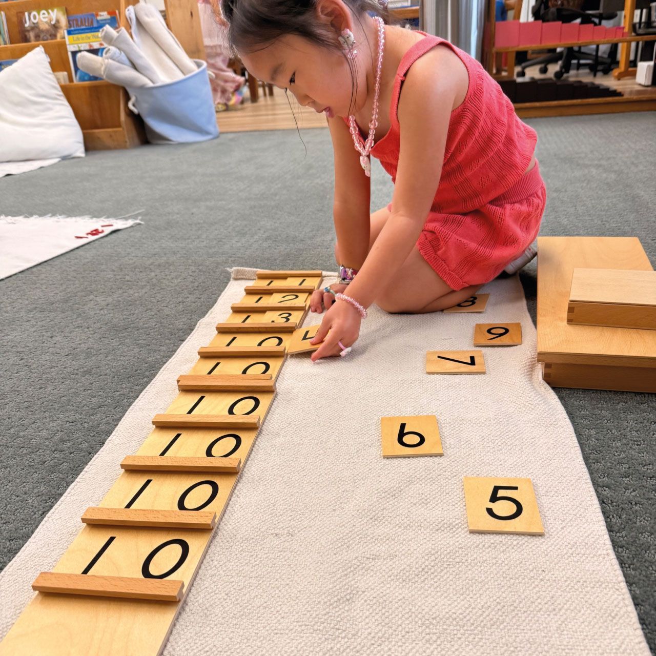A young Montessori primary student works on a floor mat with the Seguin Tens Boards, sliding wooden number cards to learn the concept of quantities and place value.