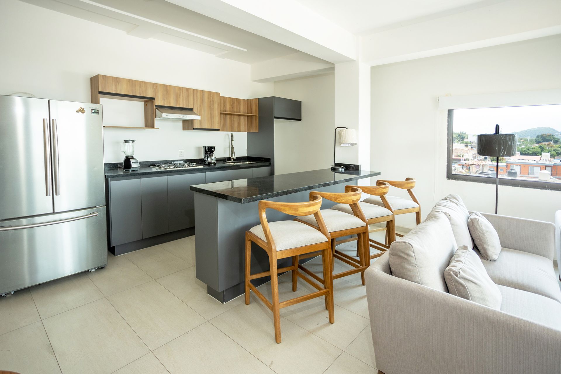 Moderna cocina y sala de estar con electrodomésticos, isla con asientos y cómodo sofá junto a la ventana.