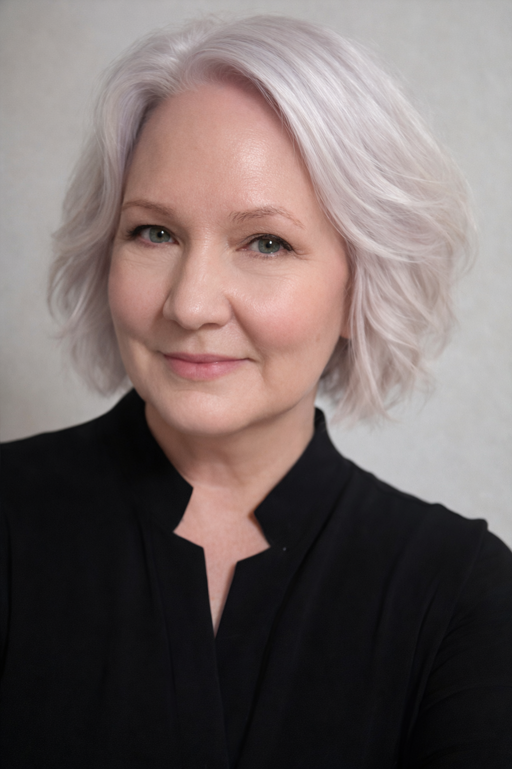 Portrait of a smiling person with short silver hair wearing a black top on a gray background