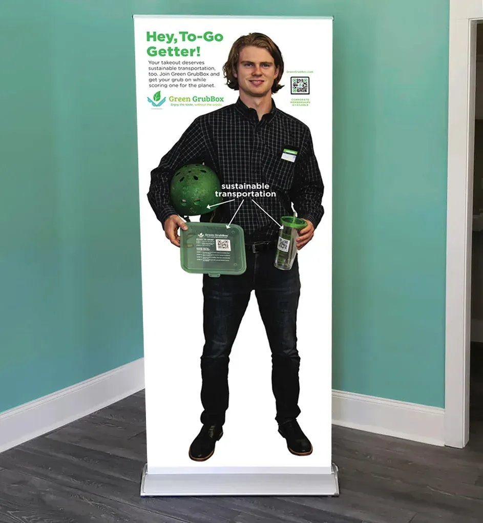 Man standing in front of a green promotional banner holding reusable shopping items