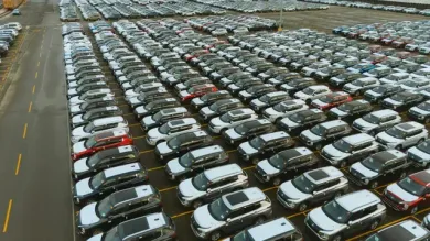 Aerial view of a vast parking lot filled with rows of white and gray cars on a wet day.