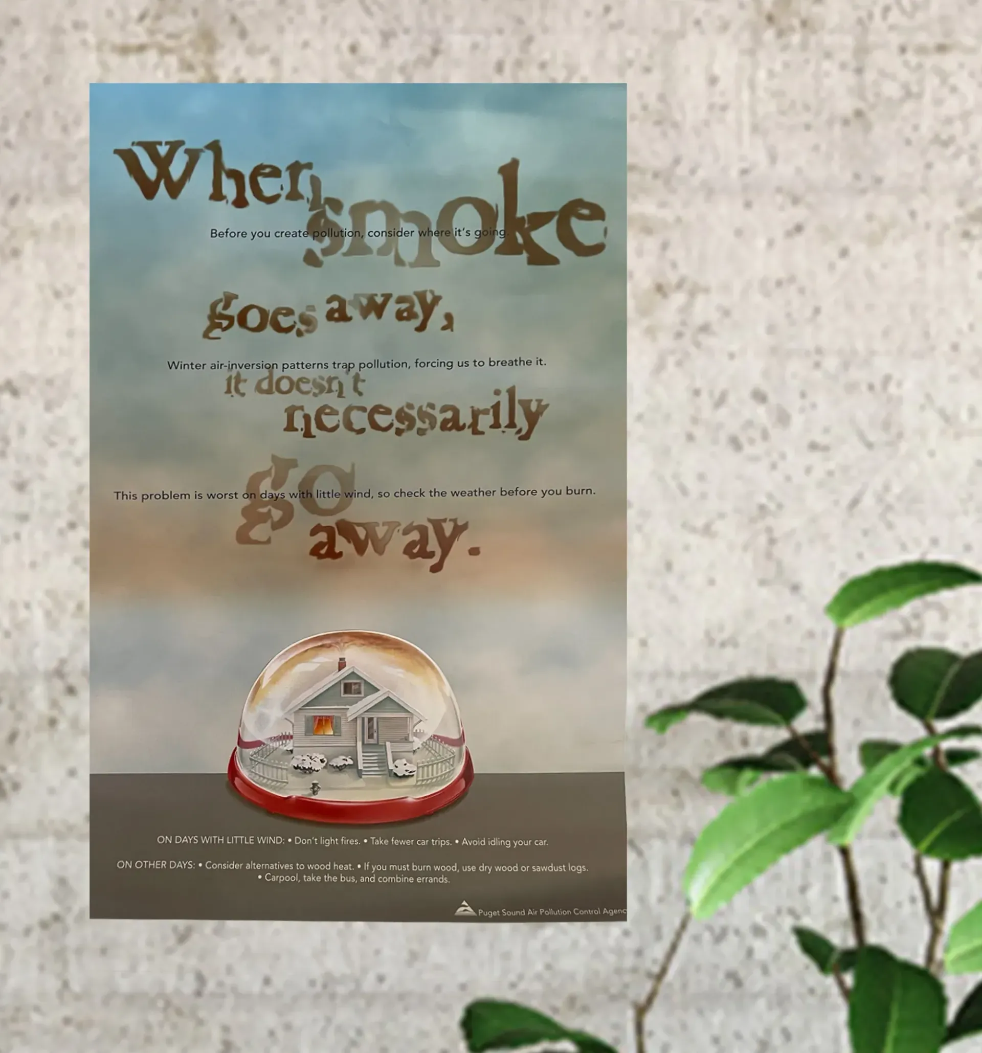 Poster with quote about smoke going away, featuring a snow globe on a beige wall next to a green plant.