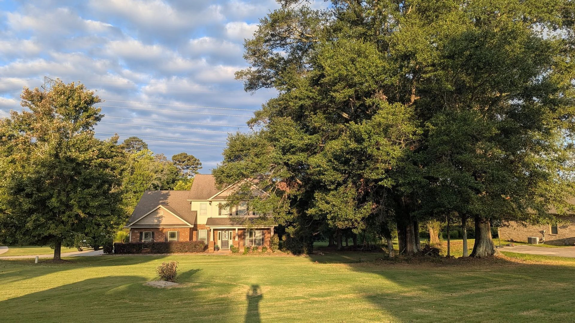 Large grassy yard with trees framing a house under a partly cloudy sky.