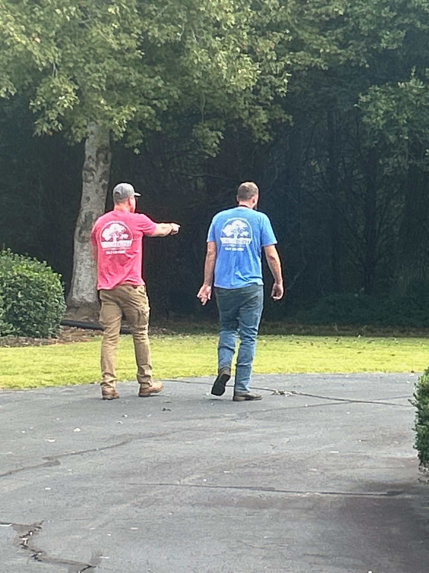 Two people walking away on a driveway beside a lawn and trees