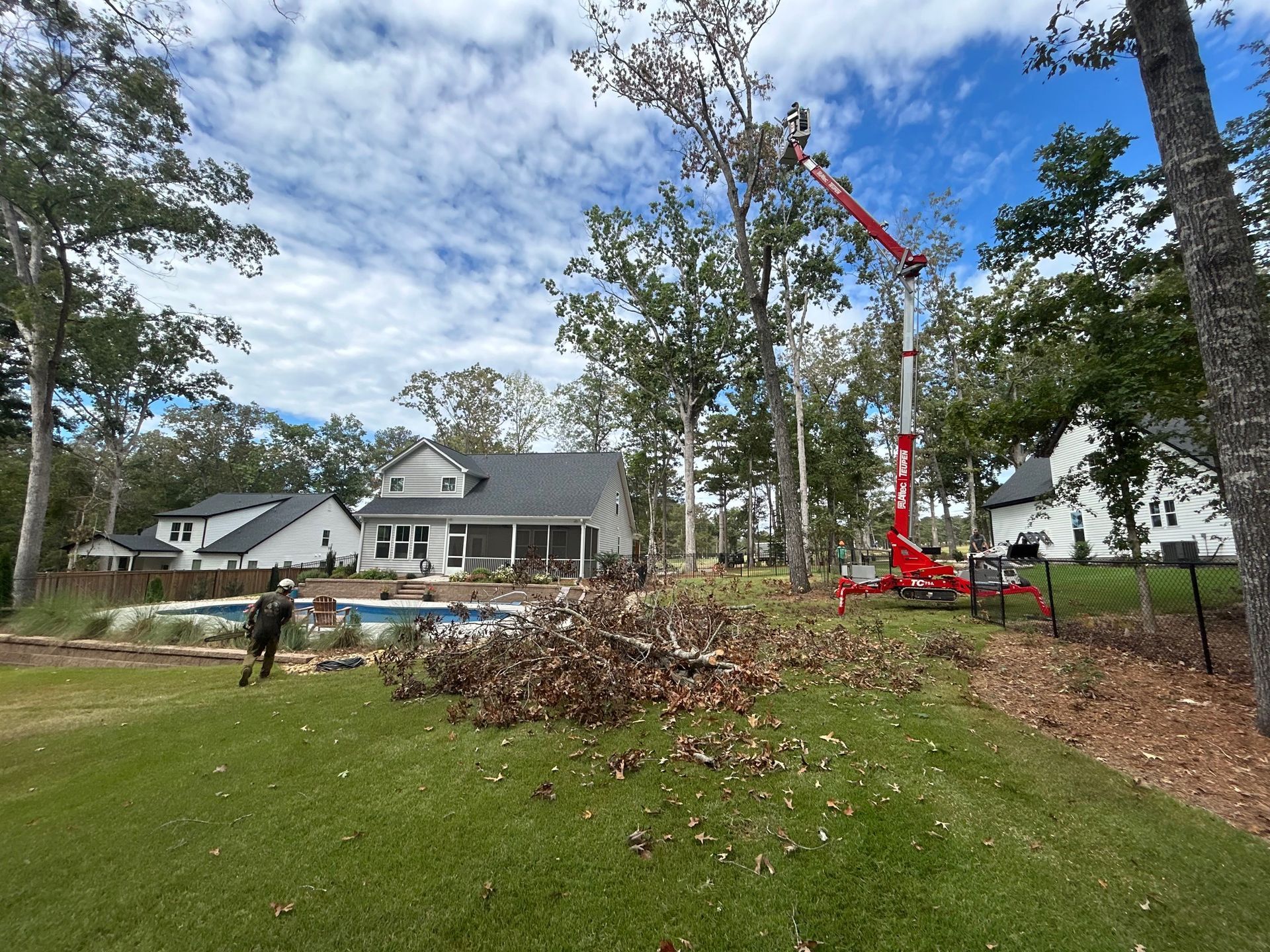 Tree removal crew with red crane clearing a large brush pile in a suburban yard