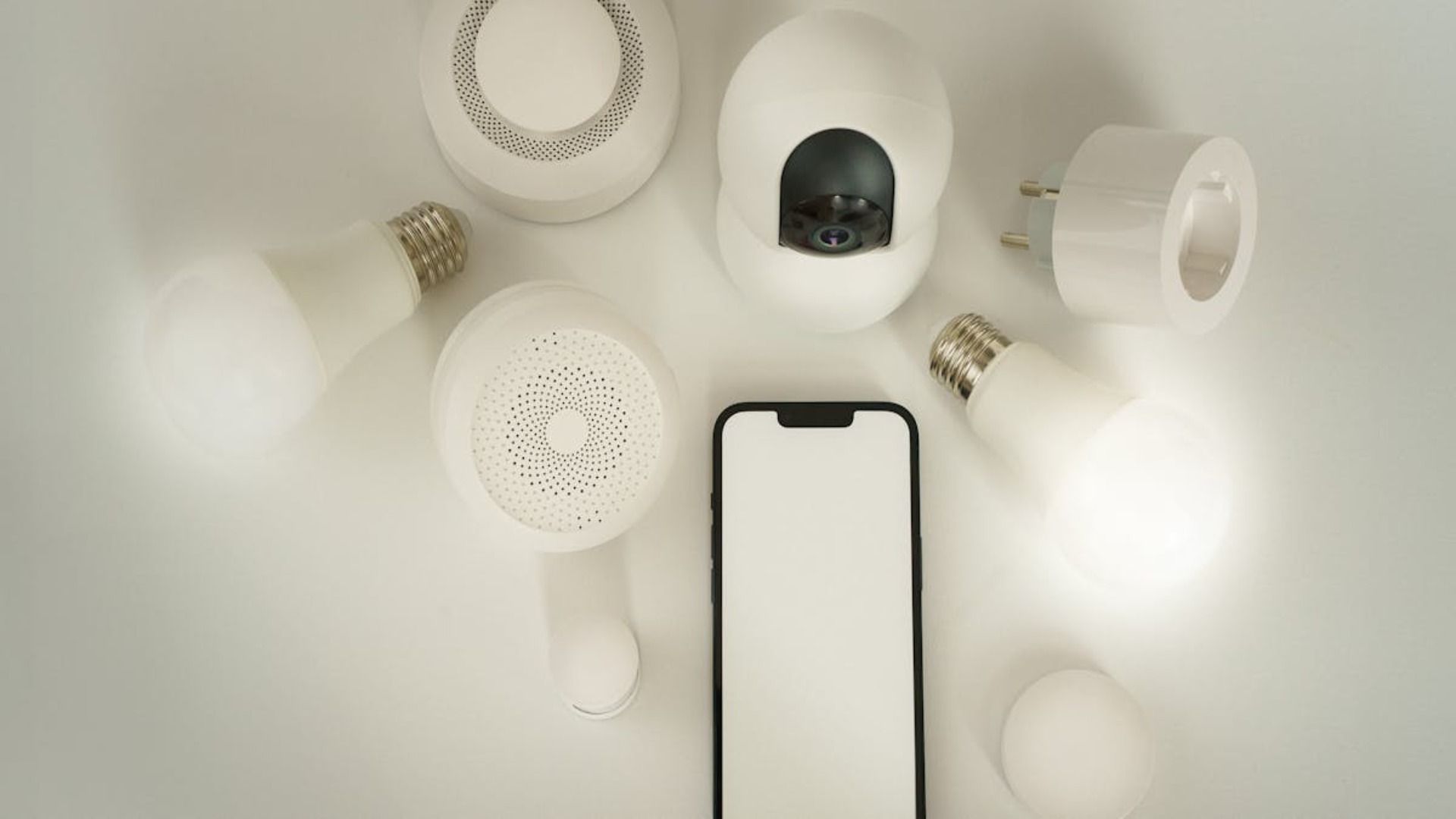 Varias bombillas blancas y un teléfono inteligente dispuestos sobre un fondo claro, vistos desde arriba.