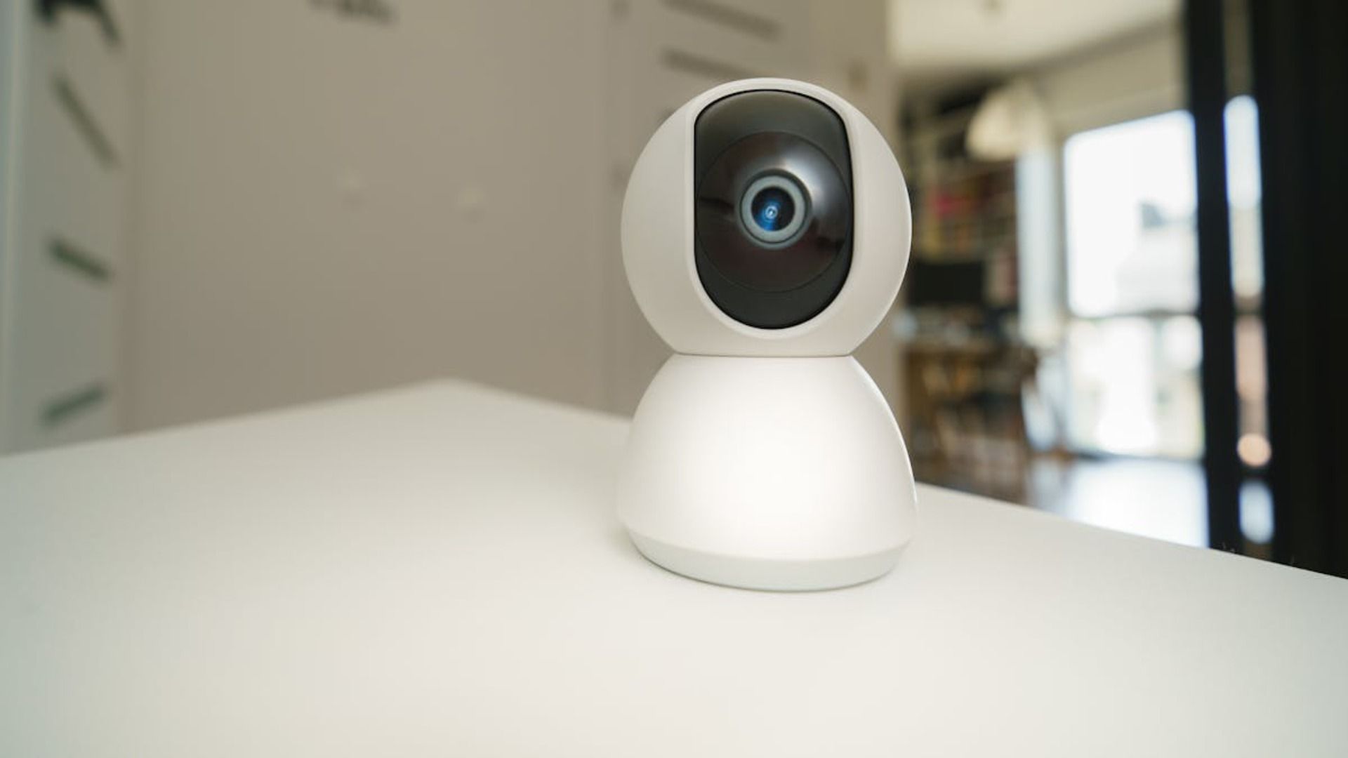 Pequeña cámara de seguridad blanca con lente negra sobre una mesa en una habitación interior luminosa.