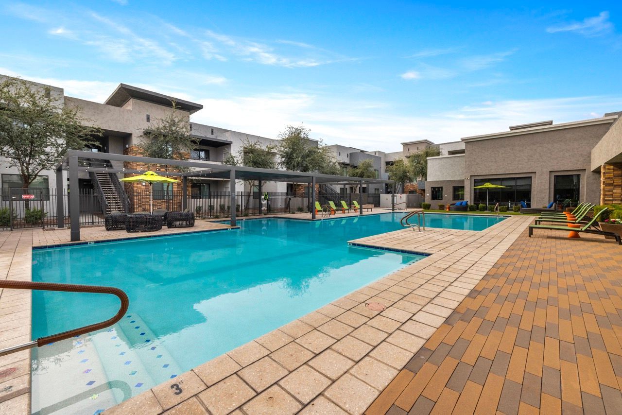 Outdoor apartment pool area with lounge chairs, umbrellas, and a brick-paved deck at Vive Apartments in Chandler, AZ. 