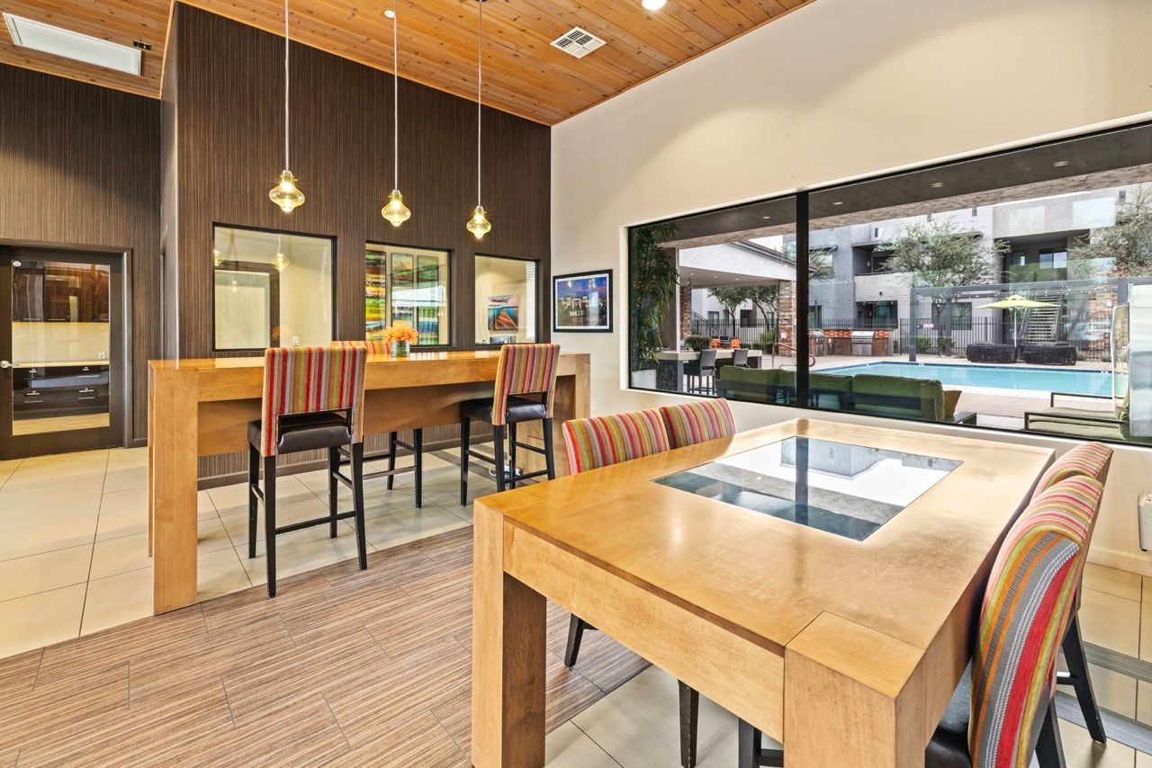 Indoor community lounge with wooden tables, striped chairs, pendant lights, and a pool view  at Vive Apartments in Chandler, AZ.