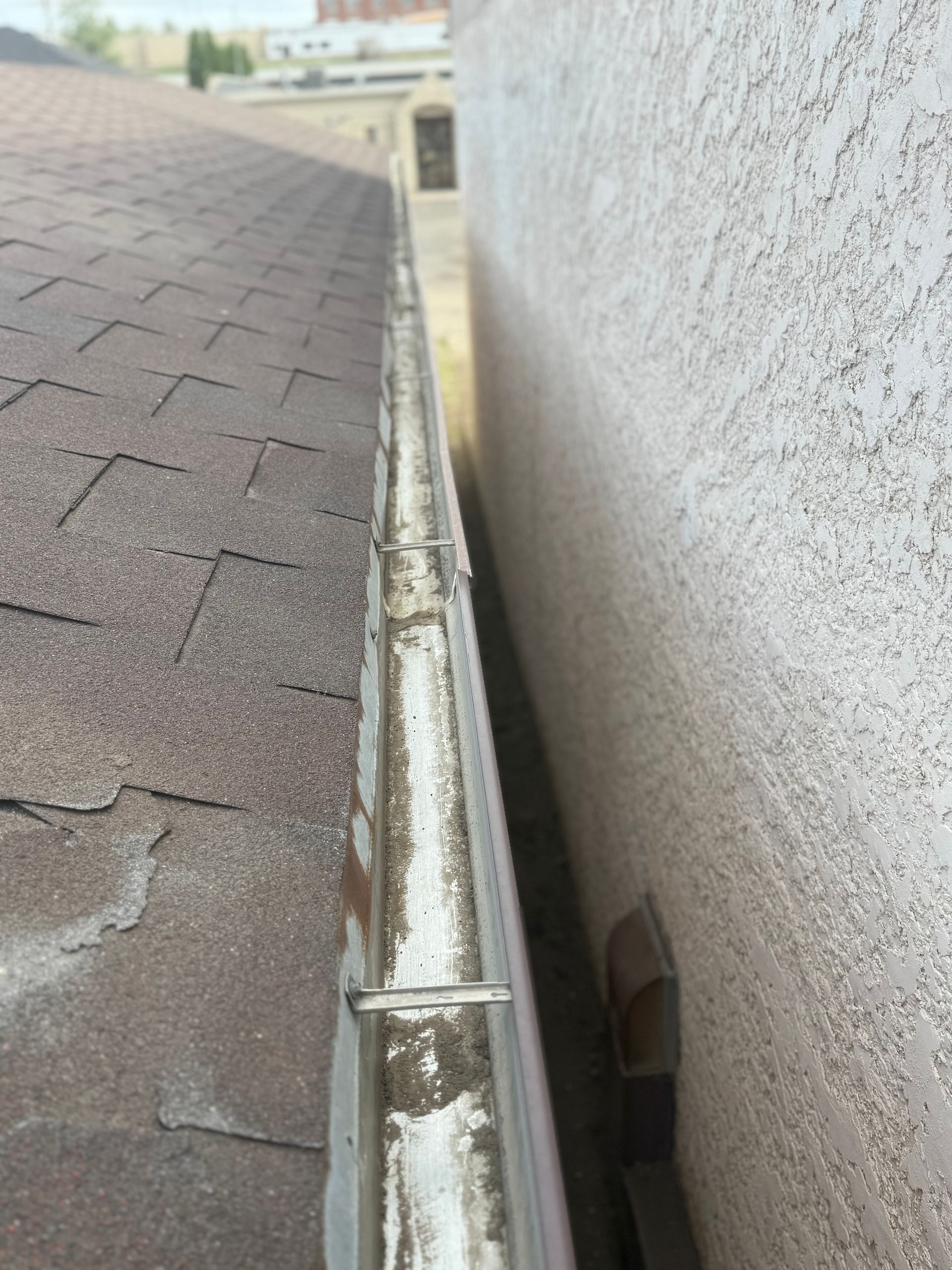View of a roof and gutter against a wall. The gutter is dirty and partially filled.