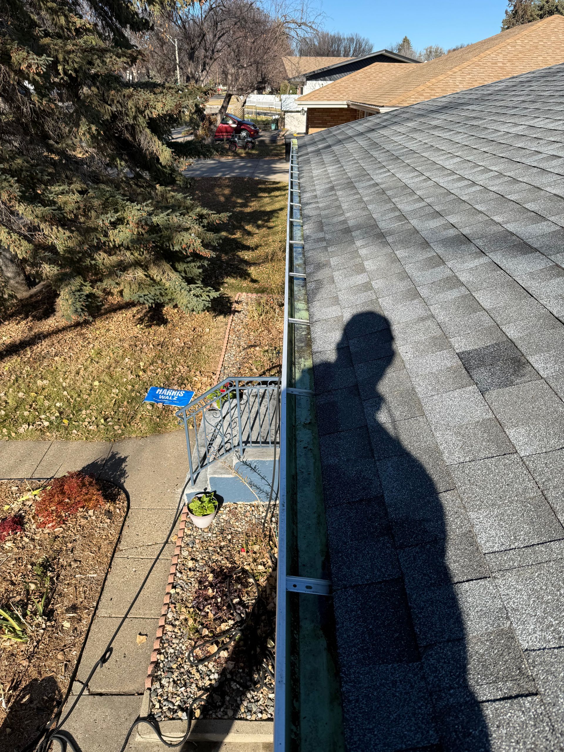 Shadow on rooftop near gutter with leaves and yard in background.