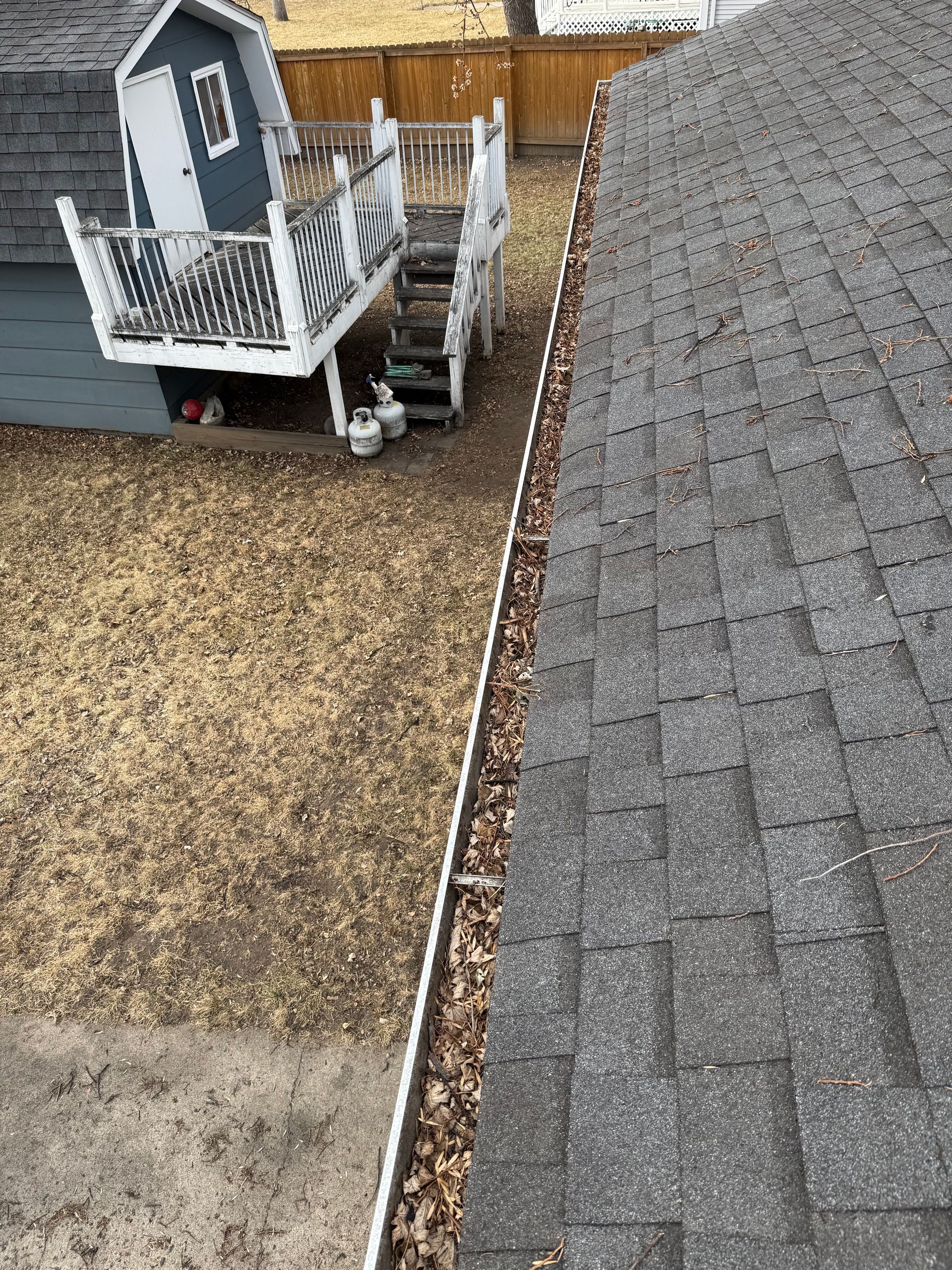 Gutter filled with leaves alongside a gray asphalt shingle roof. A playhouse is in the background.