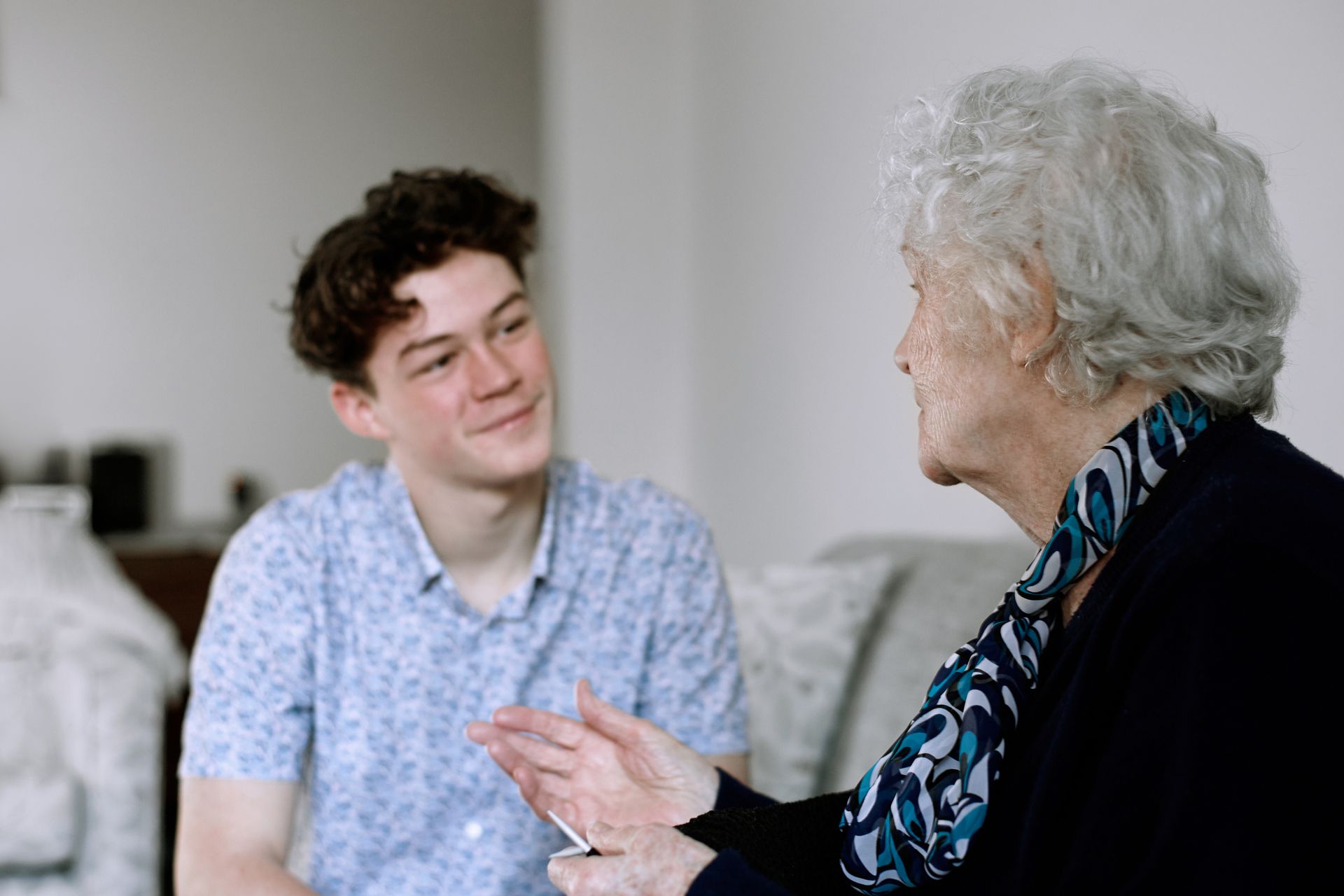 Young person smiles at an elderly person. They are having a conversation indoors.