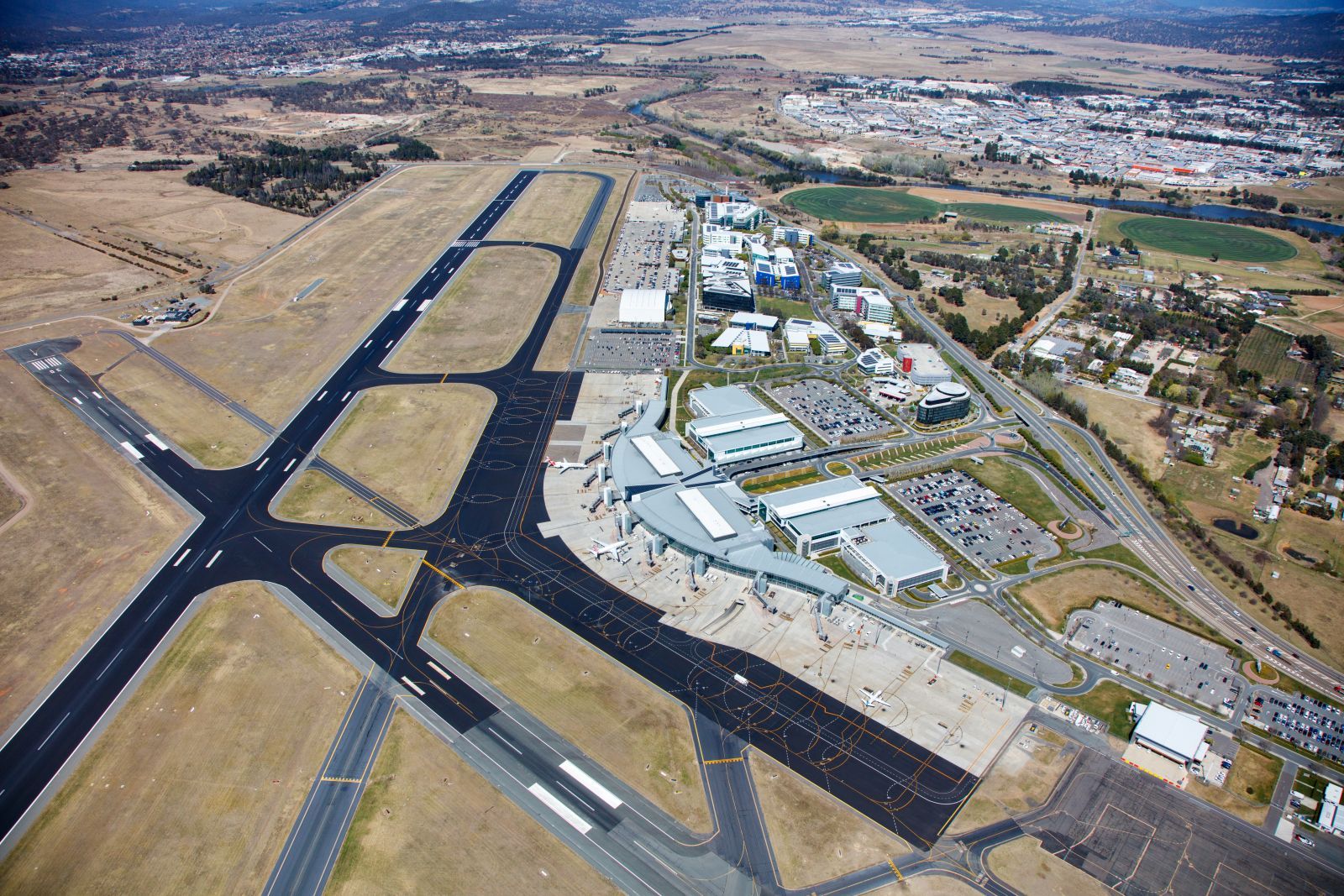 Aerial view of an airport runway and taxiways beside buildings and dry terrain