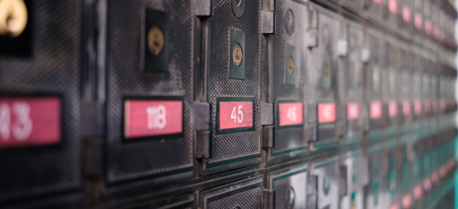 Rows of black metal mailboxes with red number labels in a blurred hallway