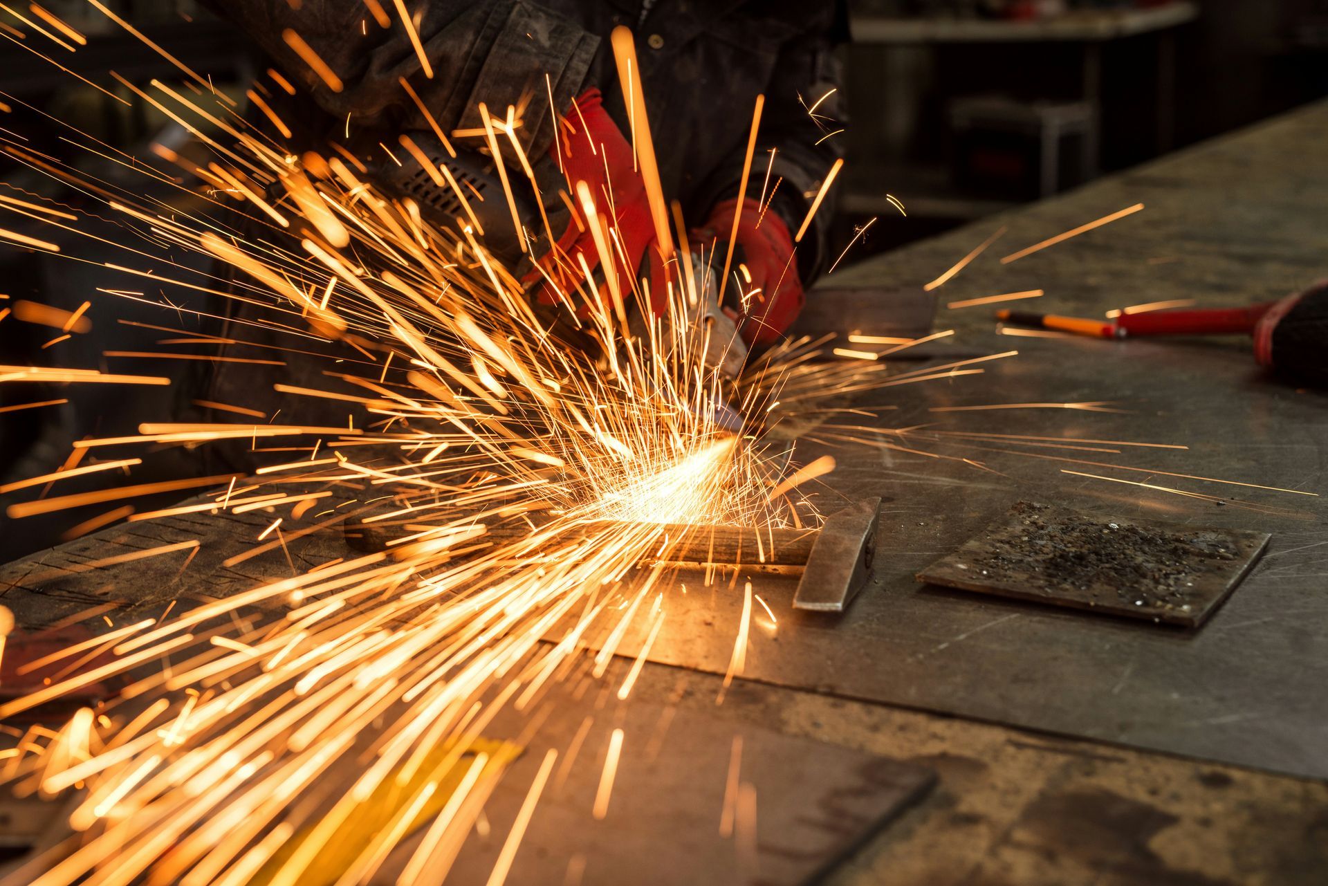Metal grinding on a workbench, sending bright orange sparks across a dim workshop floor