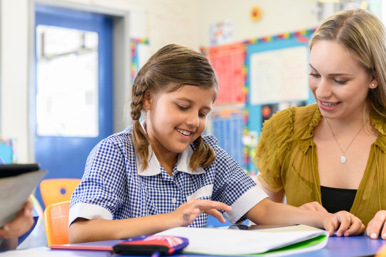 Teacher helping student read at a classroom table