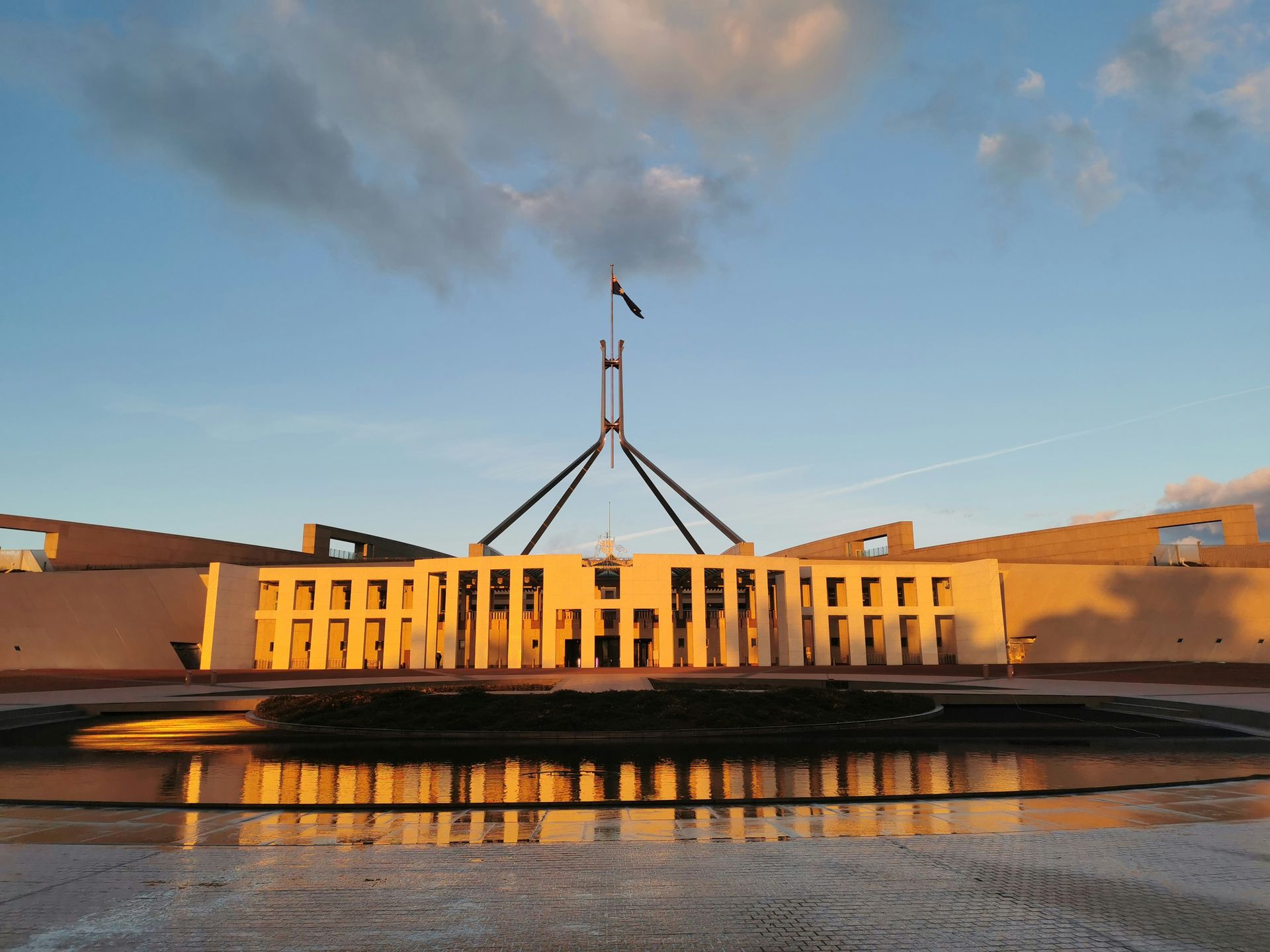 Parliament building at sunset with golden facade, reflecting in water under a cloudy sky