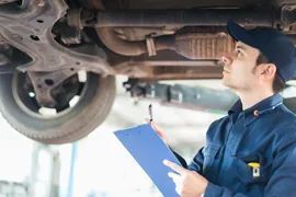 Mechanic inspecting a car’s underside with a clipboard in a garage