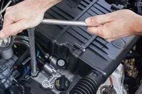 Hands using a wrench to work on a car engine under the hood.