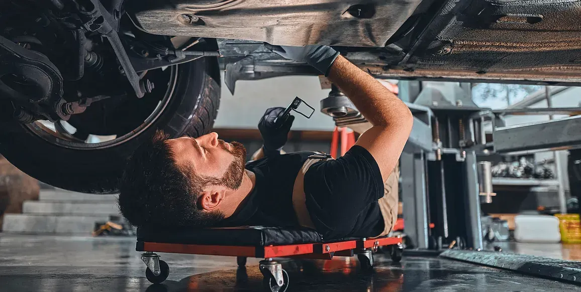 Mechanic lying under a car, using tools in an auto repair shop