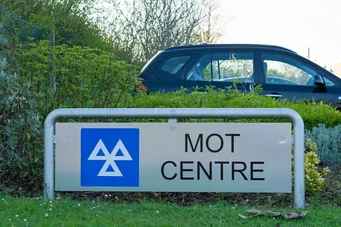 MOT Centre sign beside a parked blue car in a grassy roadside area