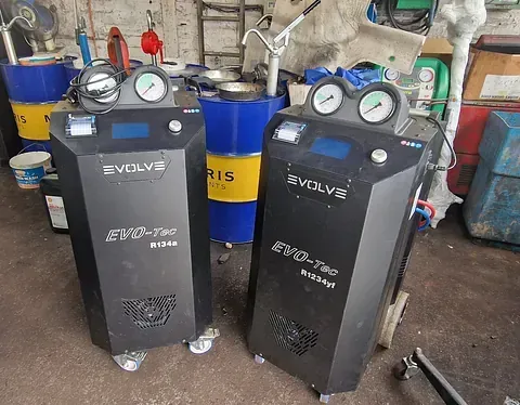 Two black EVOLVS service machines with gauges and hoses in a workshop, beside a blue barrel.