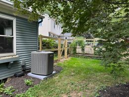 Backyard with AC unit, new wooden fence, and a grassy area next to a blue house.