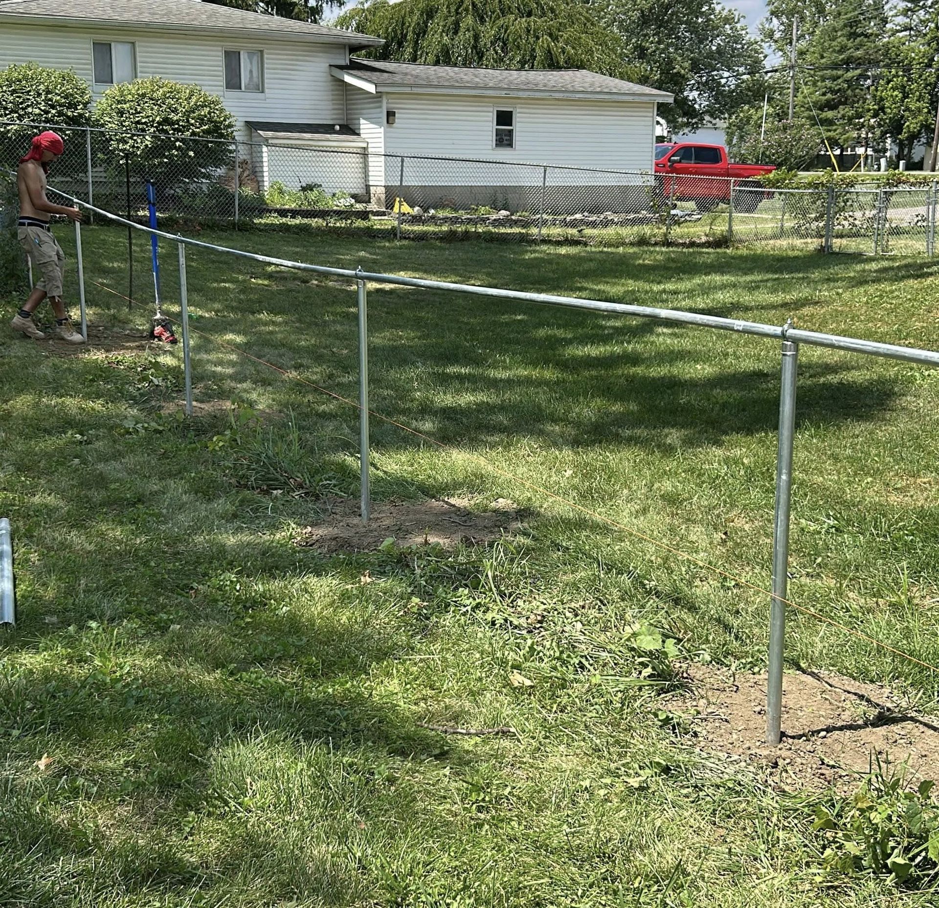 Person constructing a metal fence in a grassy backyard near a house.