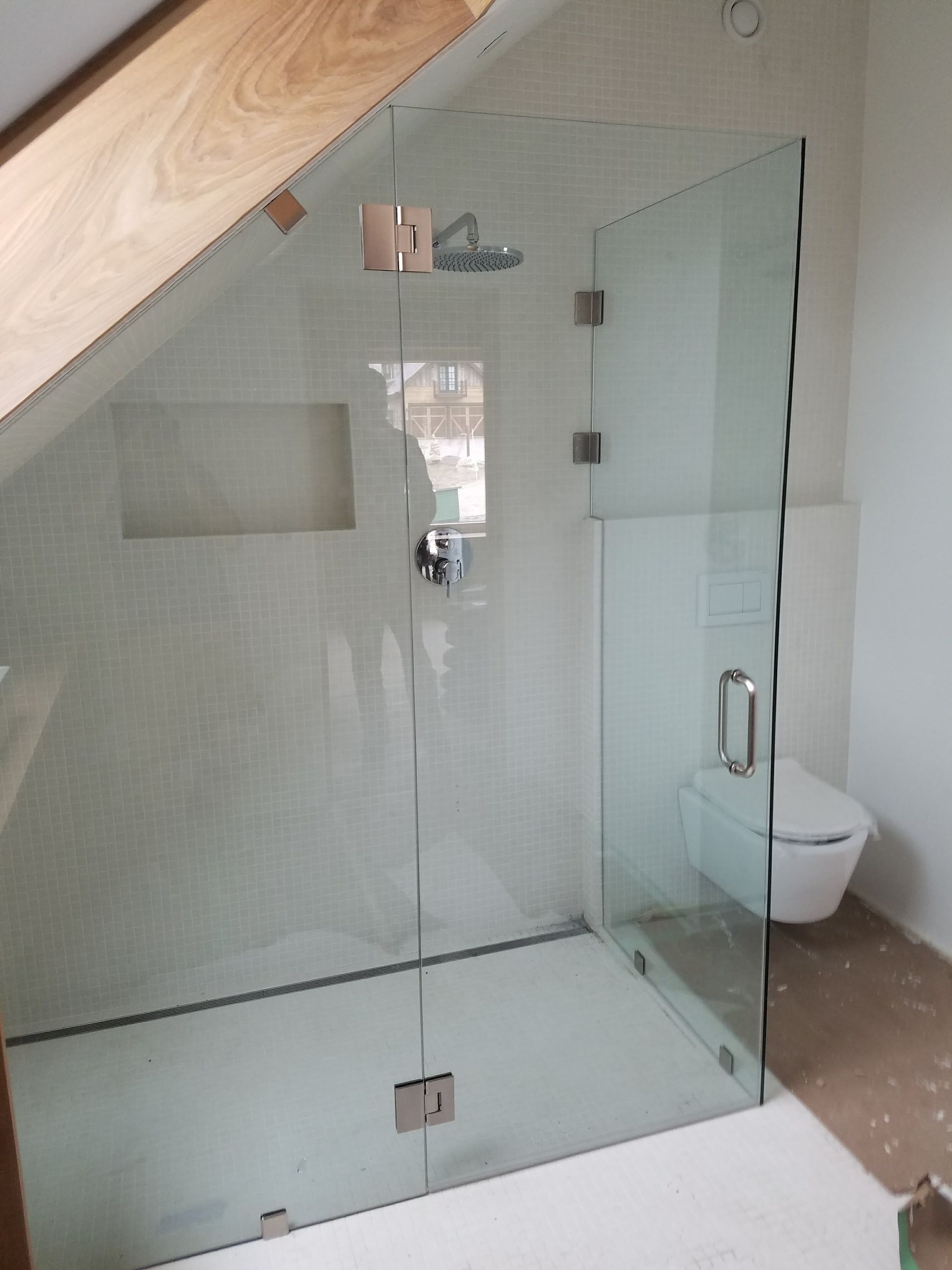 A glass shower enclosure with a door, inside a bathroom. The walls are tiled.