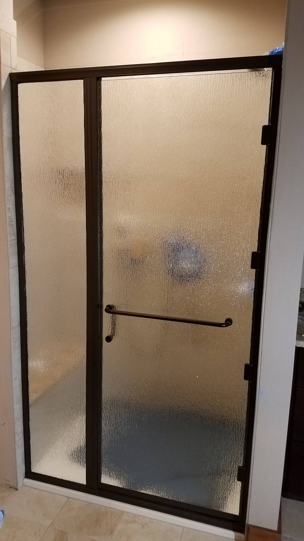 Brown-framed shower door with textured glass. It's in a bathroom with neutral walls.