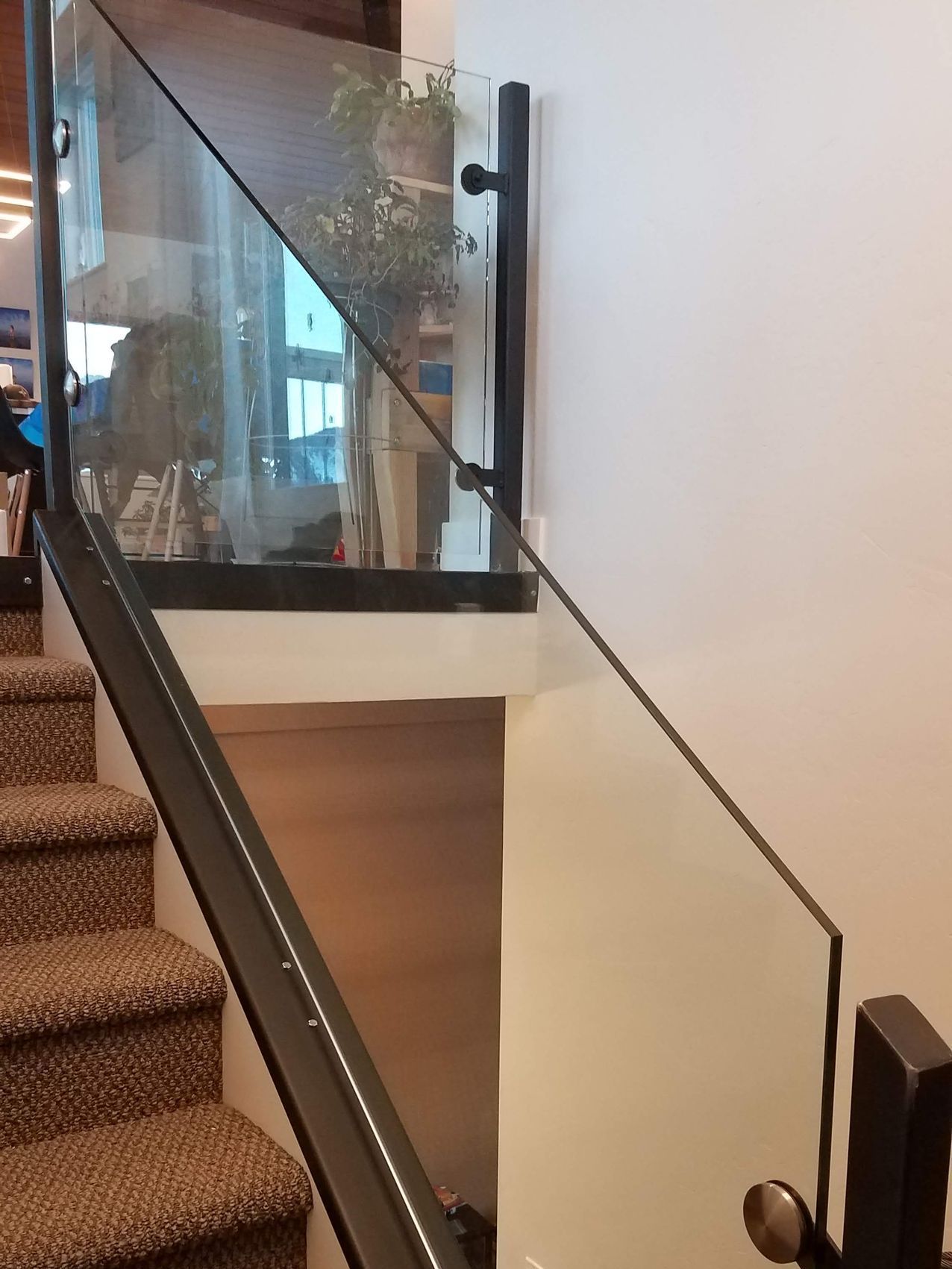Staircase with brown carpet and glass railing, black metal frame. 
