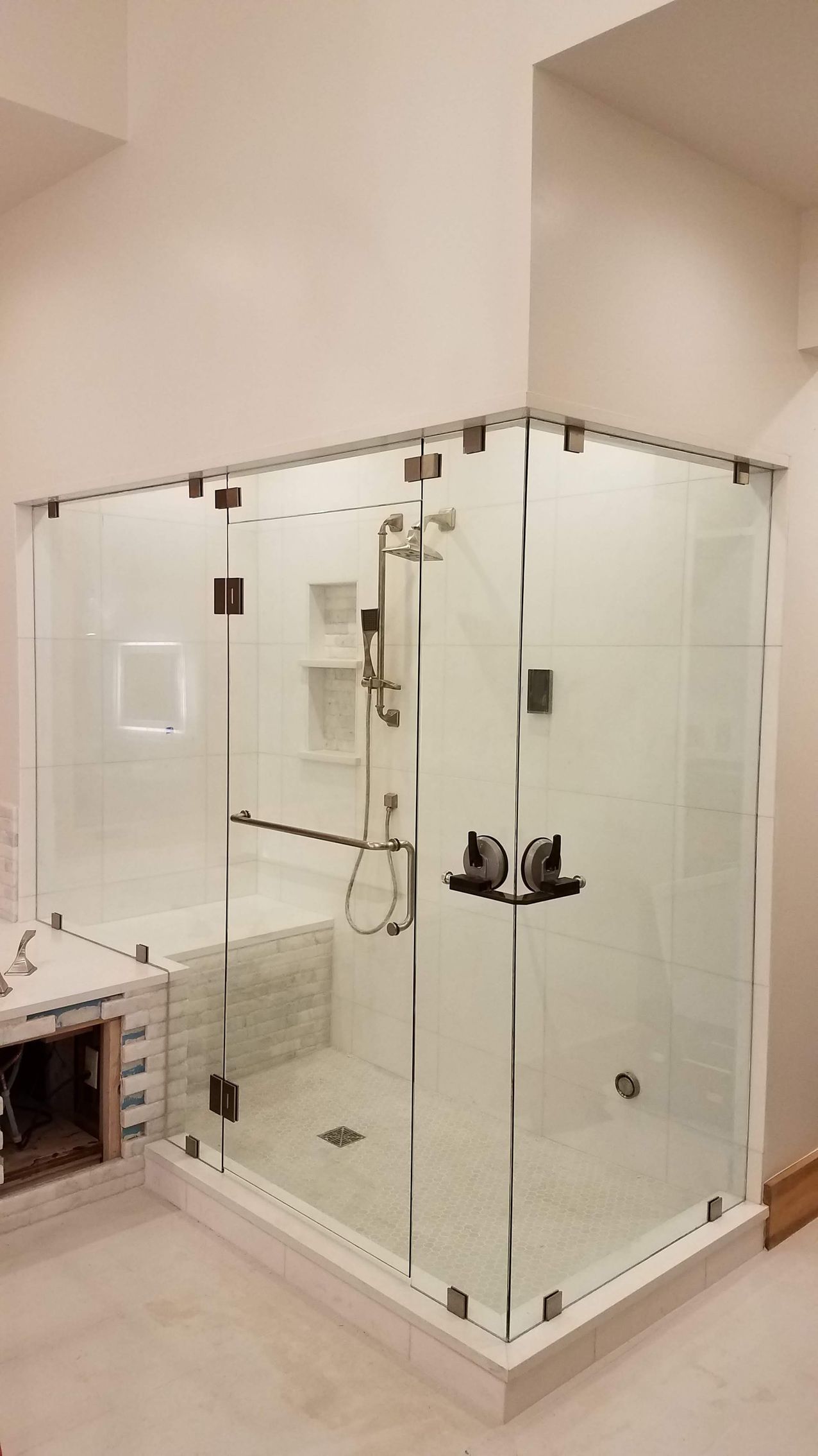 A modern, glass-enclosed shower with chrome fixtures, white walls, and a mosaic tile accent.
