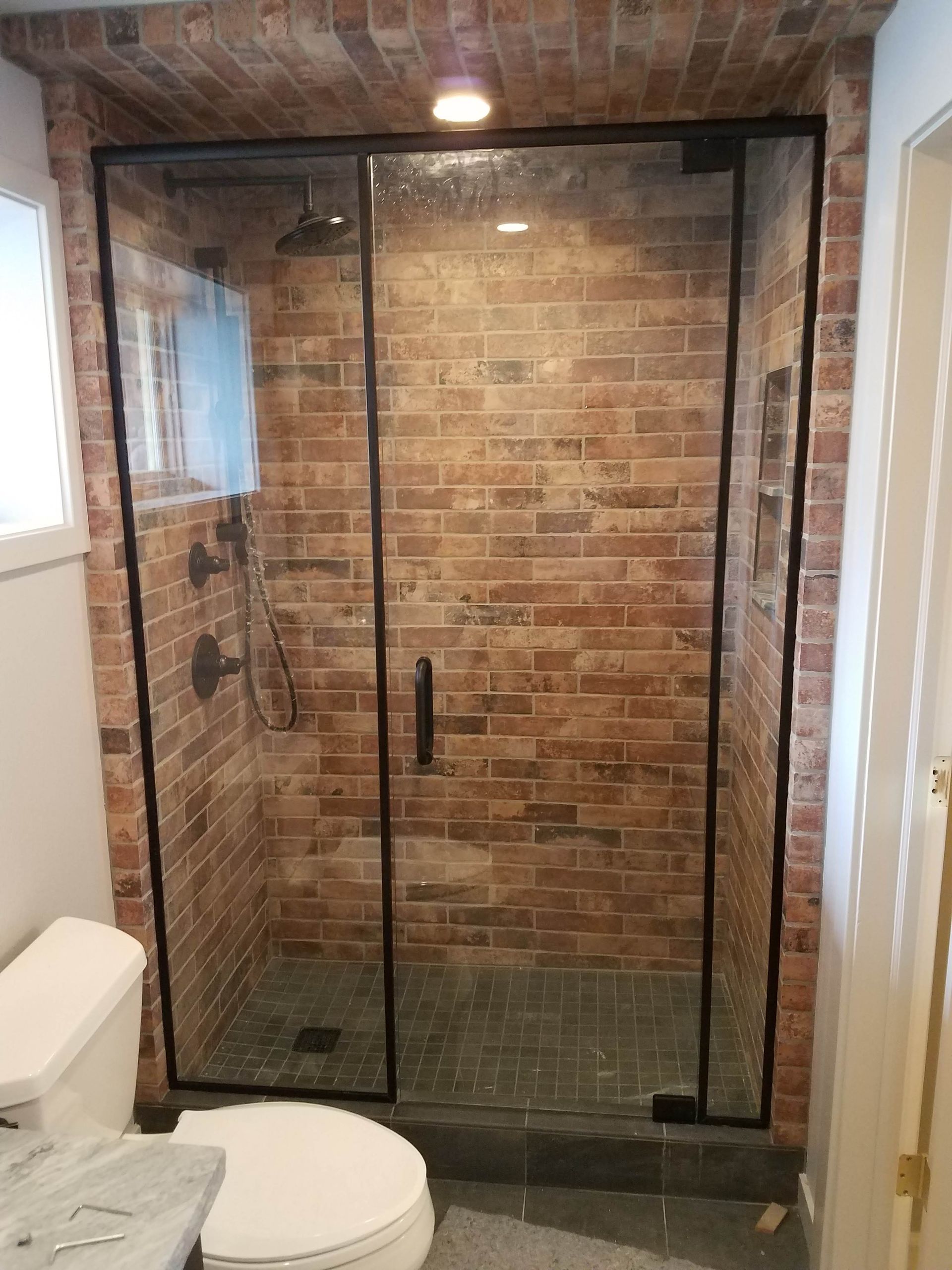 Shower with black-framed glass doors against a brick wall. A toilet is visible to the left.