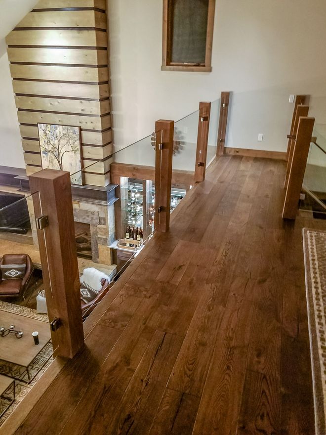 Interior view from a second floor walkway with wood flooring, glass railing, and supporting wood posts. 