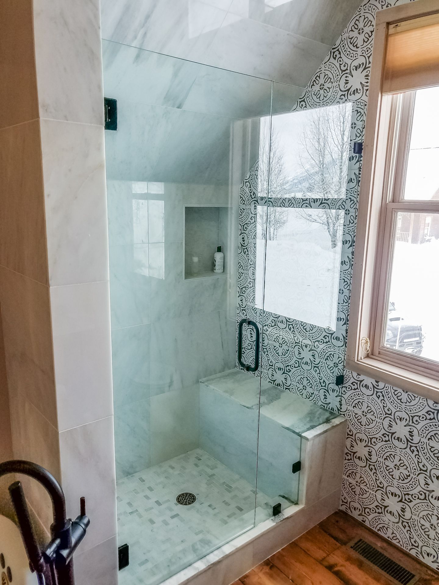 Modern shower stall with glass doors, featuring marble-look tiles and a built-in bench.