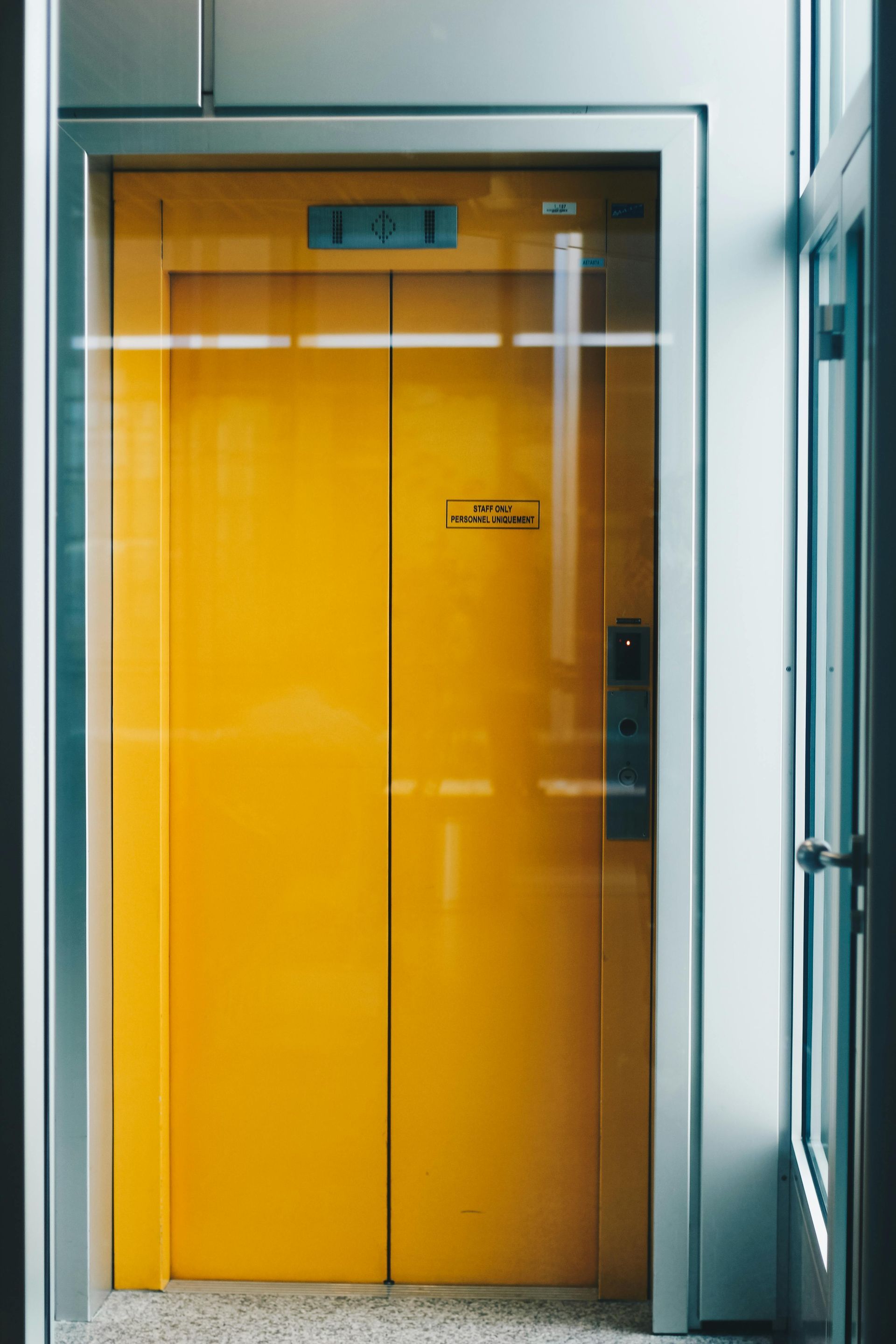 Yellow elevator doors framed by glass and a metallic border, likely in a building.