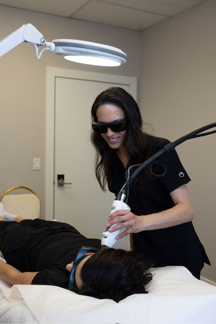 A woman is using a machine on a patient 's face.