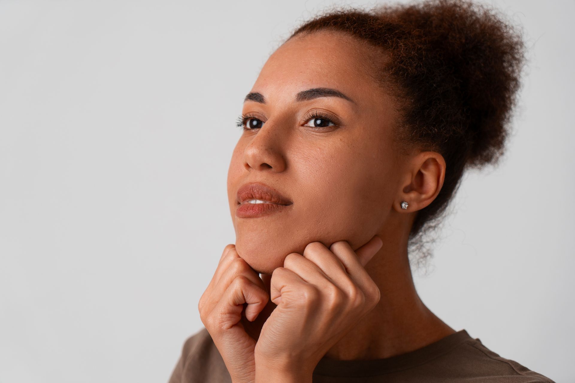 A woman is holding her chin with her hands and looking up.