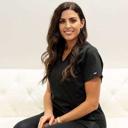 A woman in a black scrub top is sitting on a white couch.