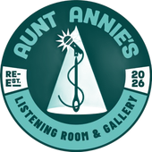 Round teal logo: "Aunt Annie's Listening Room & Gallery." A microphone and needle within a spotlight. "Re-Est. 2026."
