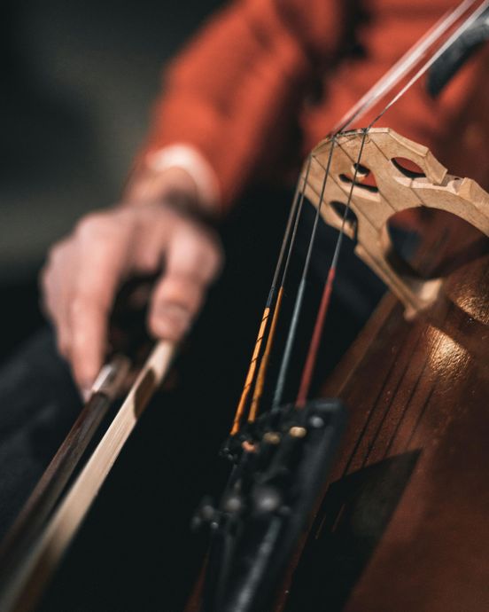 Close-up of a person playing a cello, bow drawn across the strings; red sleeve visible.