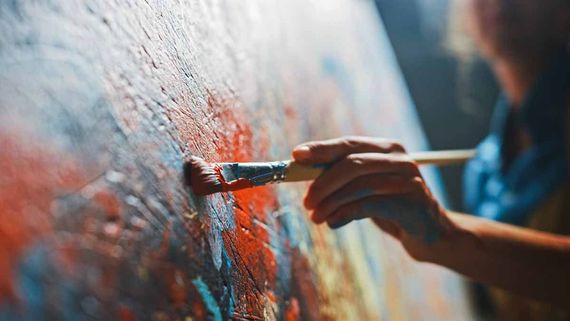 Person's hand painting with a brush on a colorful canvas.
