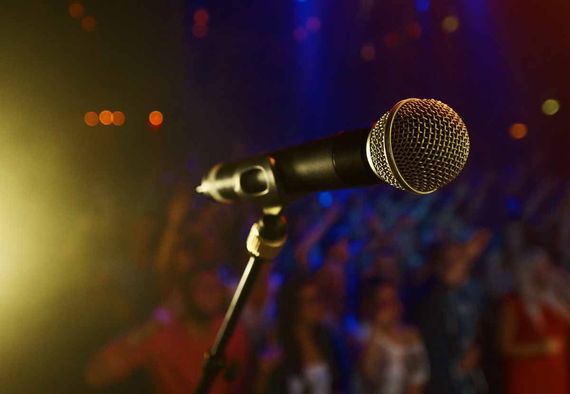 Microphone on stage with blurred crowd in background, lit by colorful stage lights.
