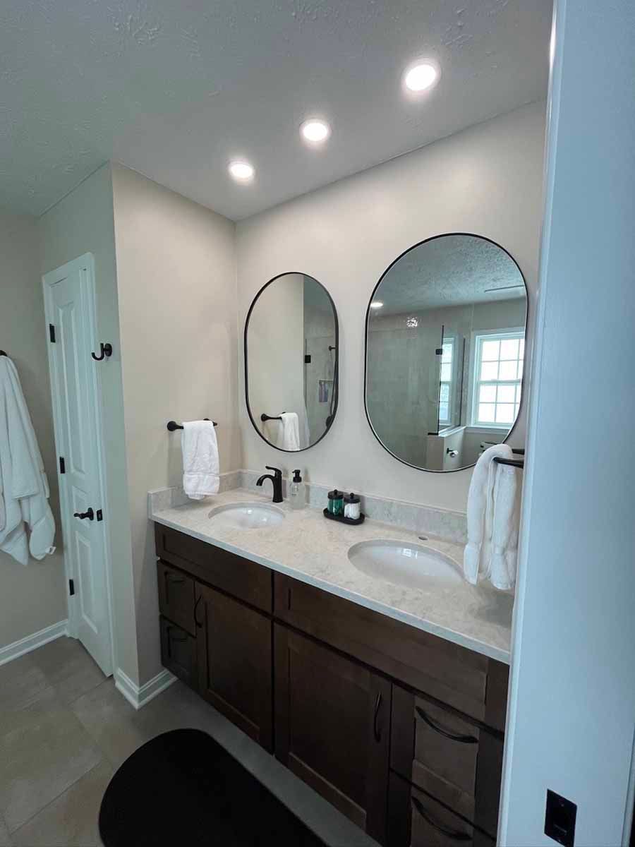 Bright bathroom vanity with double mirrors, dark cabinets, white countertop, and recessed lighting.