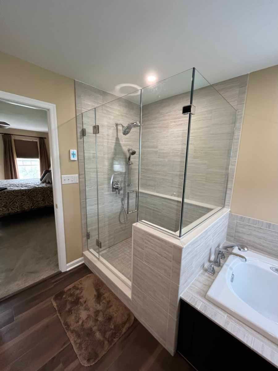 Modern bathroom with walk-in glass shower, beige tile, and dark wood floor beside a vanity sink