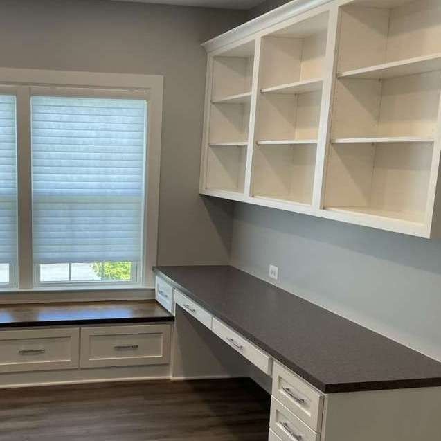 Modern home office with gray walls, built-in white shelves, dark desk, and window bench storage