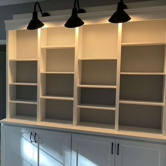 White built-in shelving with three black wall lamps above a cabinet in a home interior.